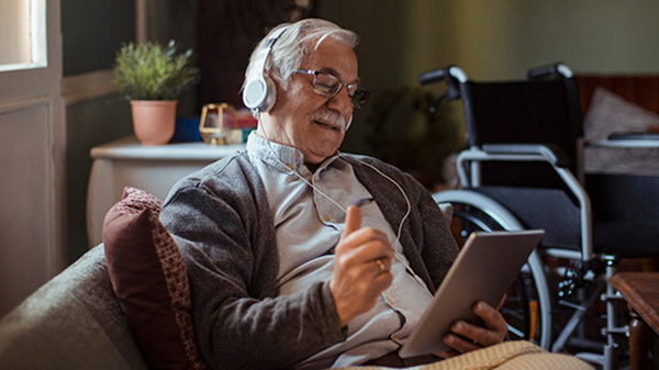 Older male with glasses has headphones on while using a tablet