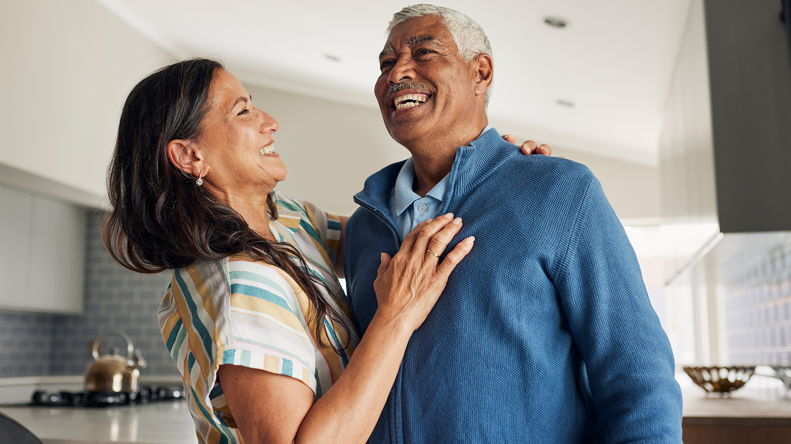 Older couple hugging and smiling in kitchen