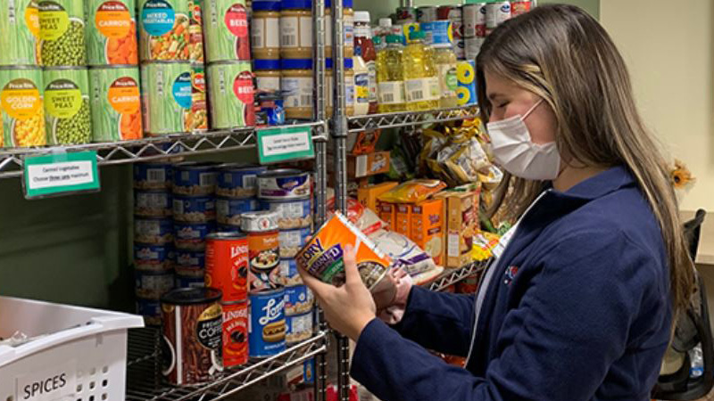 Woman holds a can while wearing a mask within Eat Well Food Farmacy program
