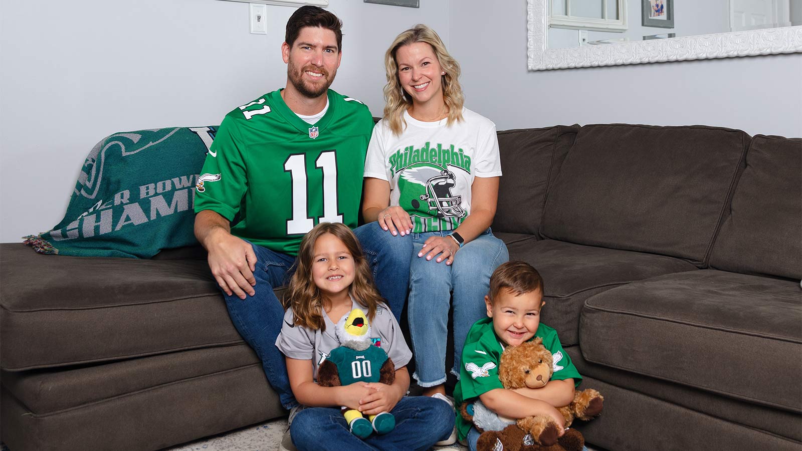 mother and father with two young children wearing Philadelphia Eagles jerseys while sitting on their couch