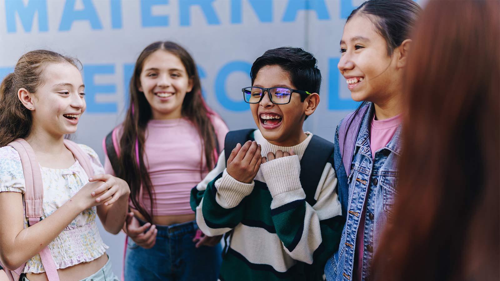 group of middle-school-aged children wearing backpacks laughing together in a group