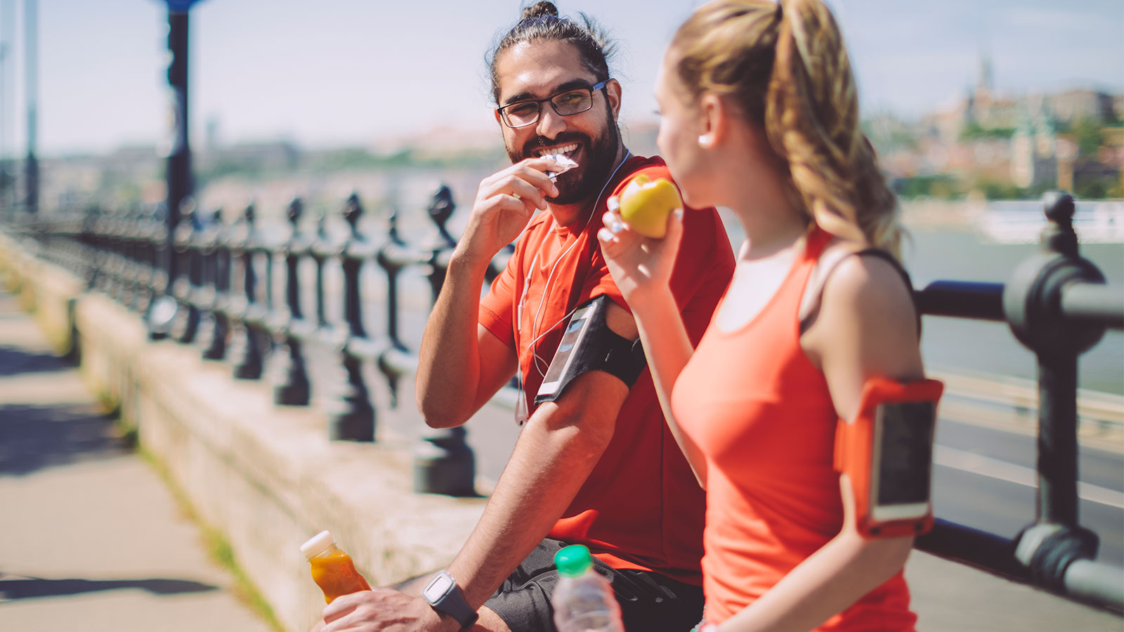 Man and woman wearing athletic clothes holding food and smiling outdoors