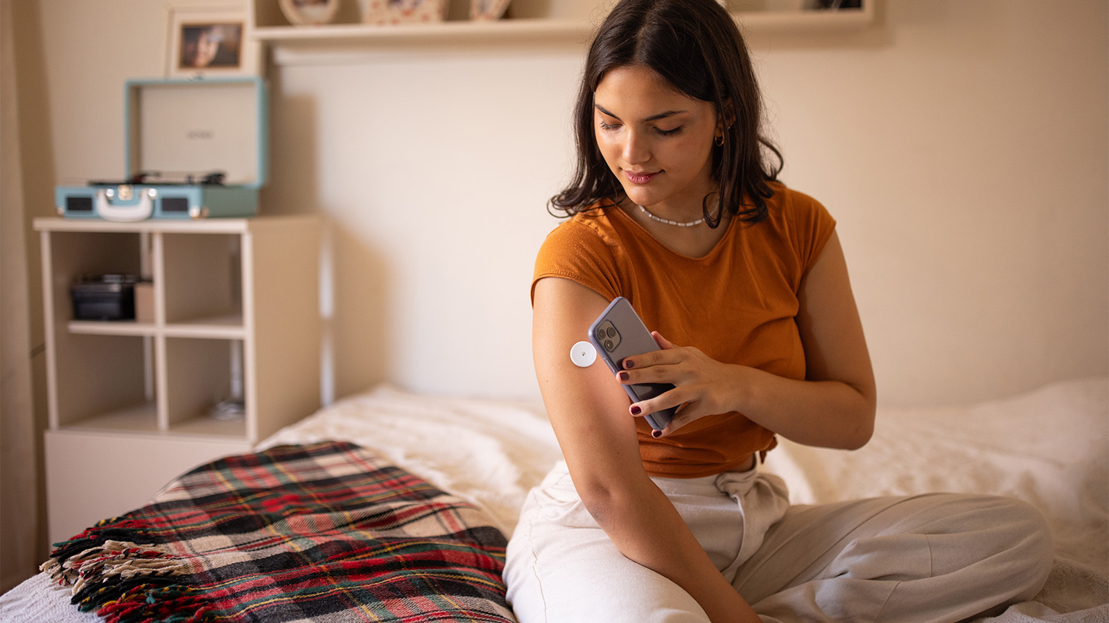 Woman in her 30s sitting on a bed and testing her blood sugar with a monitor
