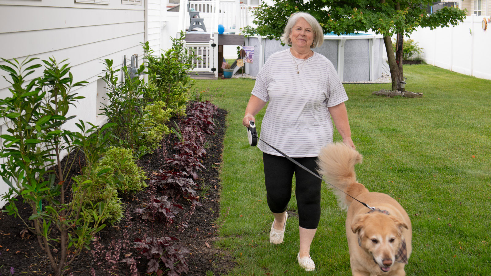 Virtua patient Teresa walks with her dog on a leash in her yard