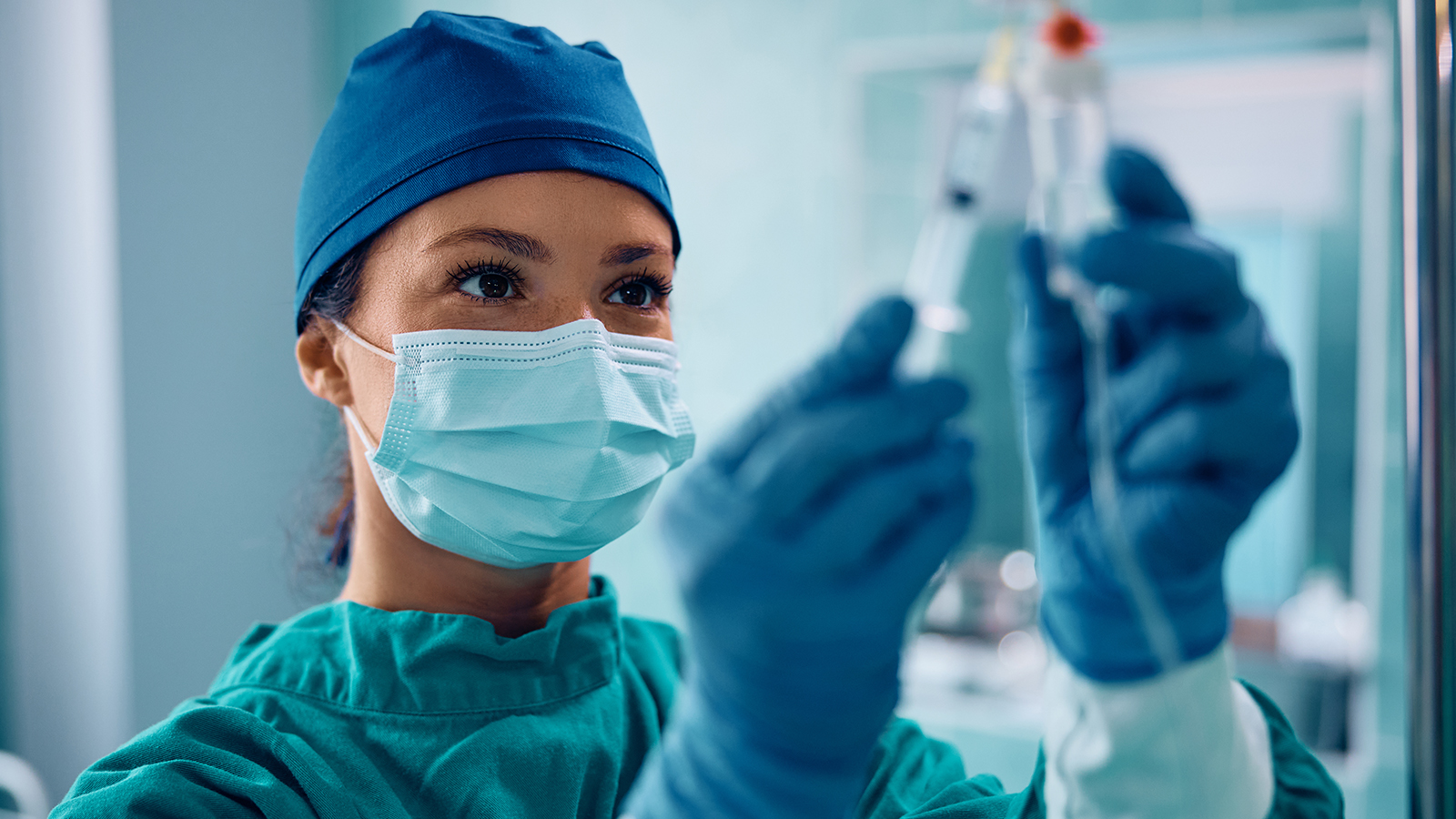 female doctor in surgical gown, gloves, and mask injecting liquid into an IV drip