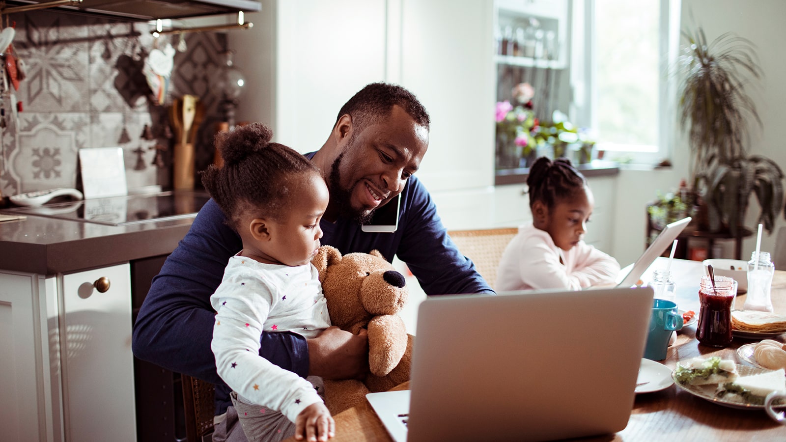 A father and two daughters sit at the table while looking at a laptop