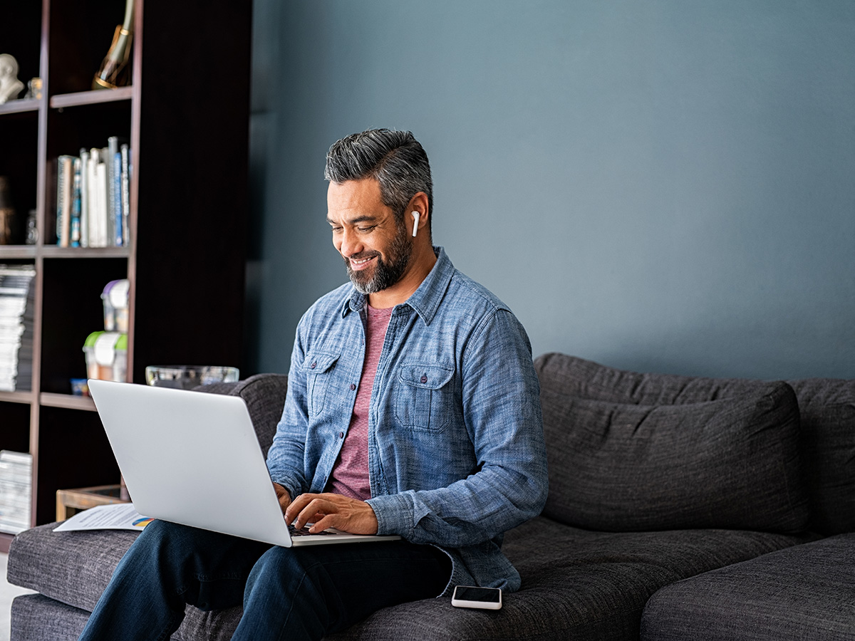 Middle age man sitting on the couch, looking at his laptop