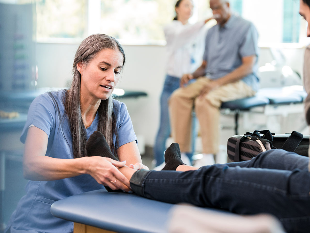 Female doctor assessing a patient's ankle on a table in a medical setting