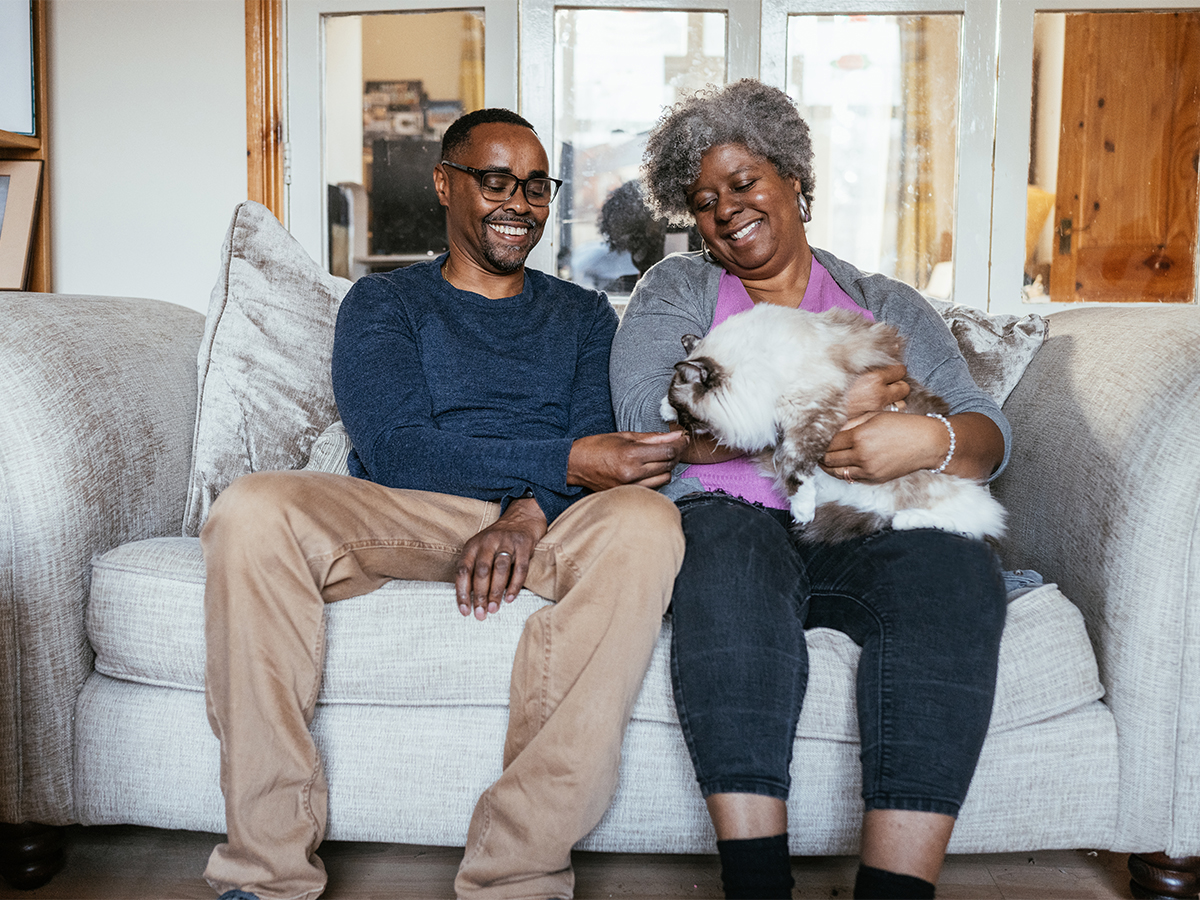 Man and woman smiling on a couch, holding a dog